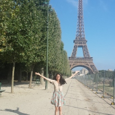 A tourist posing happily in front of the Eiffel Tower in Paris in the early morning.