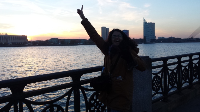 Young girl poses in front of a beautiful sun set by the River Daugava after first day of Latvian trip.