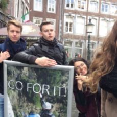 Young university students, from Germany on a road trip to Maastricht, posing next to a sign on the streets that says "Go for it!".